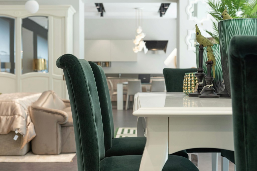 Close-up of dark green velvet dining chairs around a white table with decorative accents