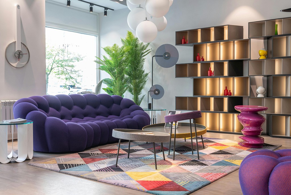 Modern living room with purple sofa, colorful rug, and open shelving