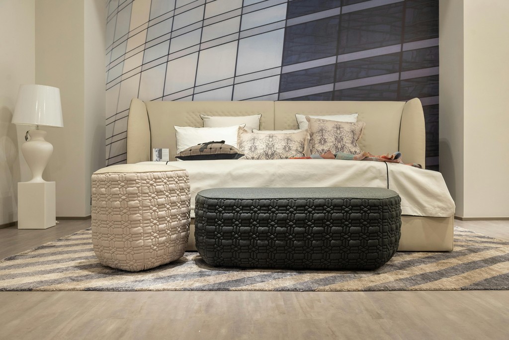 Beige upholstered bed with patterned pillows and ottomans